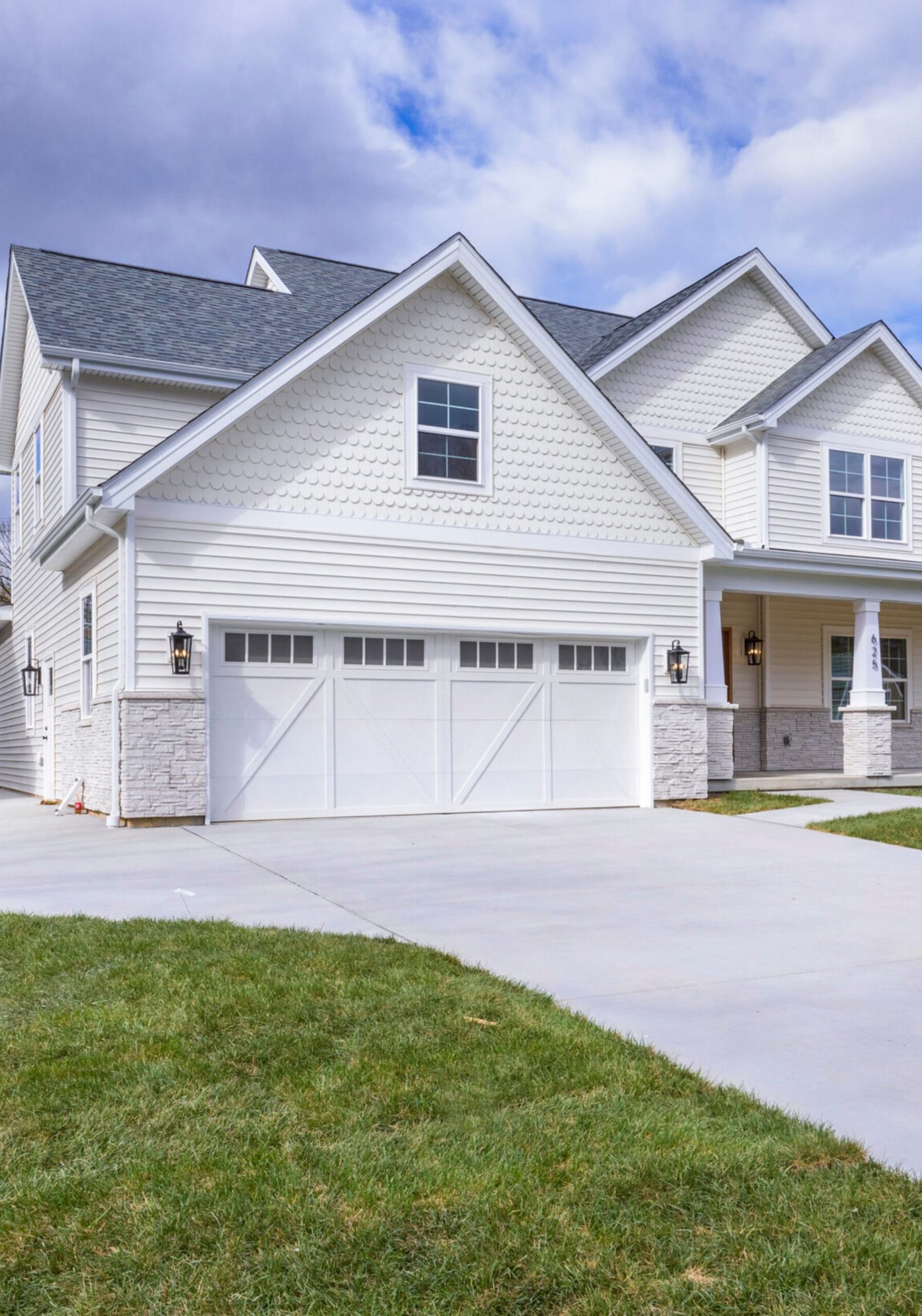 Custom home exterior by FM Design Build in St. Louis featuring white siding, decorative gables, stone accents, and a two-car garage.